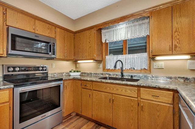 kitchen with a textured ceiling, sink, light wood-type flooring, and stainless steel appliances