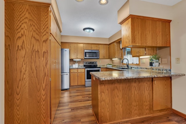 kitchen featuring kitchen peninsula, sink, stainless steel appliances, and hardwood / wood-style flooring