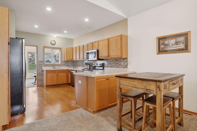 kitchen with backsplash, sink, light wood-type flooring, appliances with stainless steel finishes, and kitchen peninsula