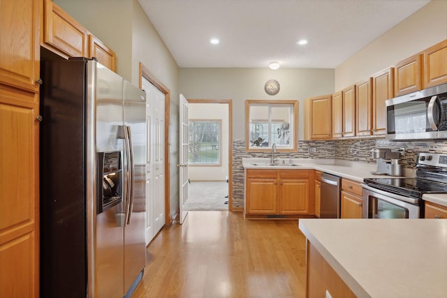 kitchen with decorative backsplash, light brown cabinetry, stainless steel appliances, sink, and light hardwood / wood-style floors