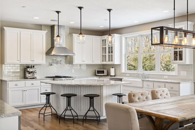 21360 Christmas Ln, Shorewood, MN 55331 - kitchen featuring a center island, white cabinetry, wall chimney exhaust hood, a sink, and wood finished floors