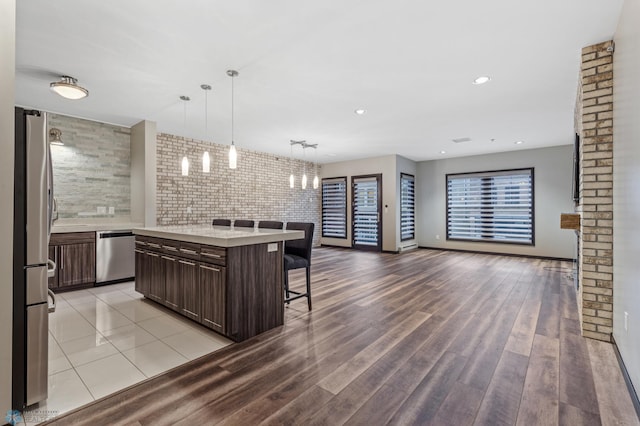 kitchen featuring appliances with stainless steel finishes, dark brown cabinets, light hardwood / wood-style flooring, hanging light fixtures, and a breakfast bar area