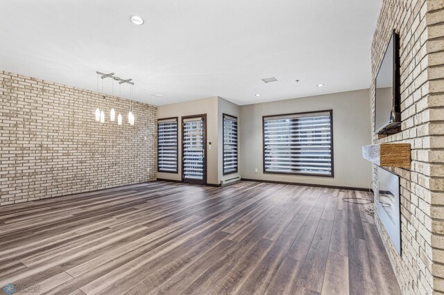 unfurnished living room with rail lighting, dark wood-type flooring, and brick wall