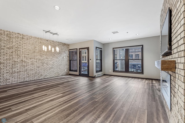 unfurnished living room with dark hardwood / wood-style floors, track lighting, and brick wall