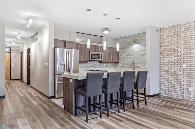 kitchen featuring hanging light fixtures, stainless steel appliances, dark brown cabinets, and light hardwood / wood-style flooring