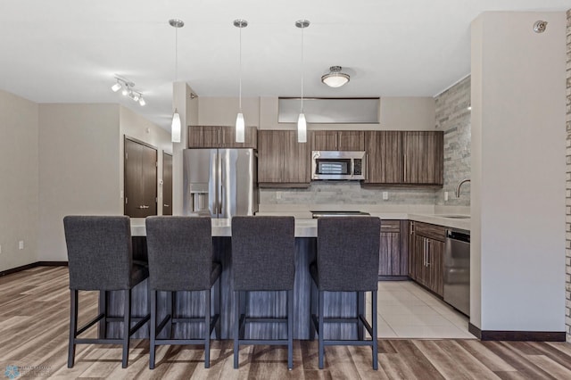 kitchen with a center island, decorative light fixtures, light hardwood / wood-style flooring, dark brown cabinets, and stainless steel appliances