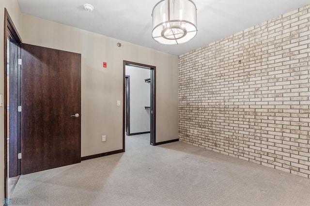 empty room featuring light carpet, brick wall, and an inviting chandelier