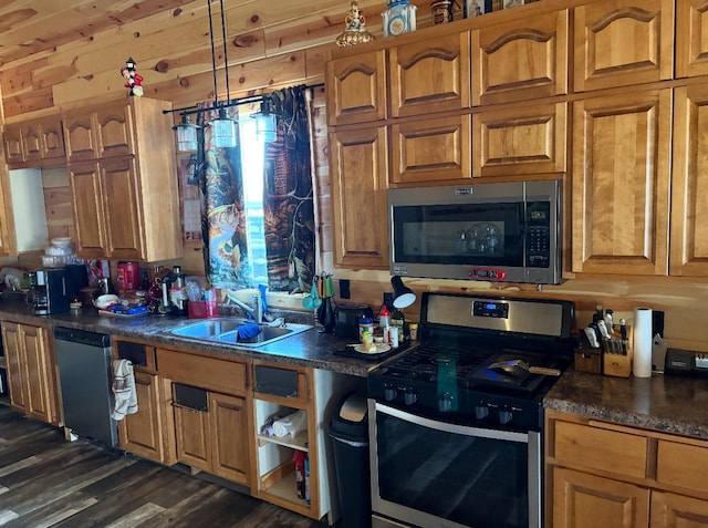 kitchen featuring appliances with stainless steel finishes, dark hardwood / wood-style flooring, sink, decorative light fixtures, and wood walls