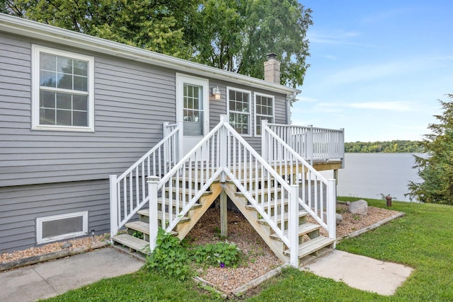 property entrance with a chimney, a deck with water view, and a lawn