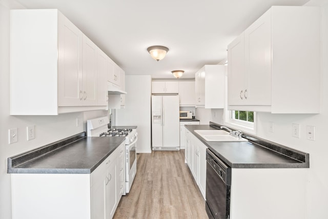 kitchen featuring dark countertops, white appliances, white cabinets, and a sink