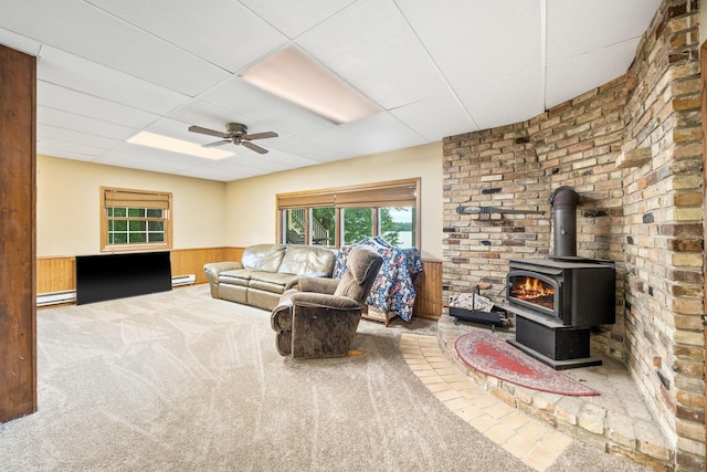 living room with wainscoting, a wood stove, carpet, a paneled ceiling, and wood walls