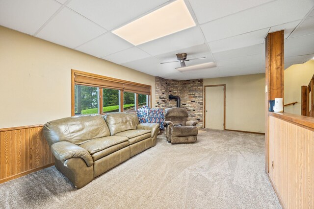 living room featuring wainscoting, a wood stove, carpet flooring, a paneled ceiling, and wood walls