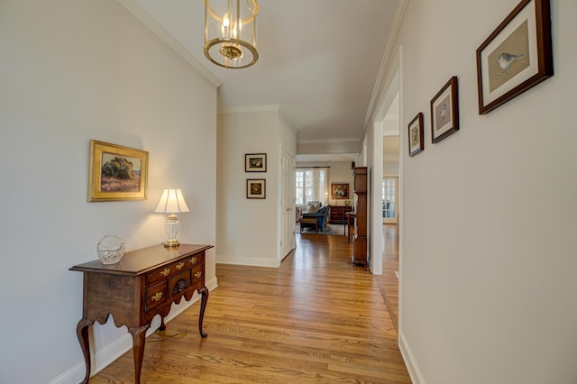 hall with light wood-type flooring, baseboards, a chandelier, and ornamental molding