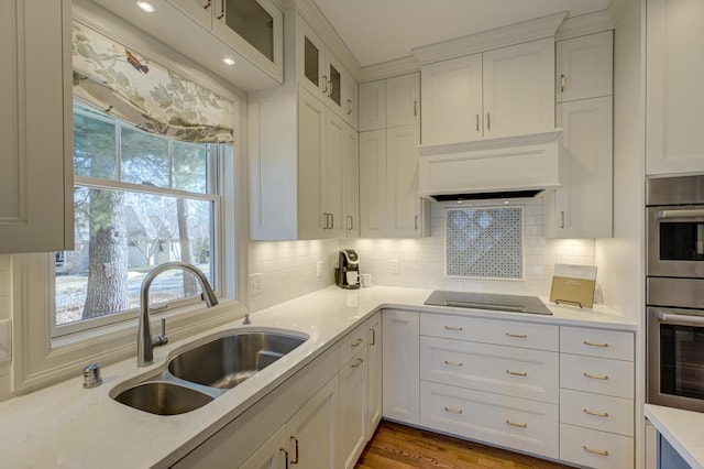 kitchen featuring a sink, black electric stovetop, white cabinetry, and custom range hood