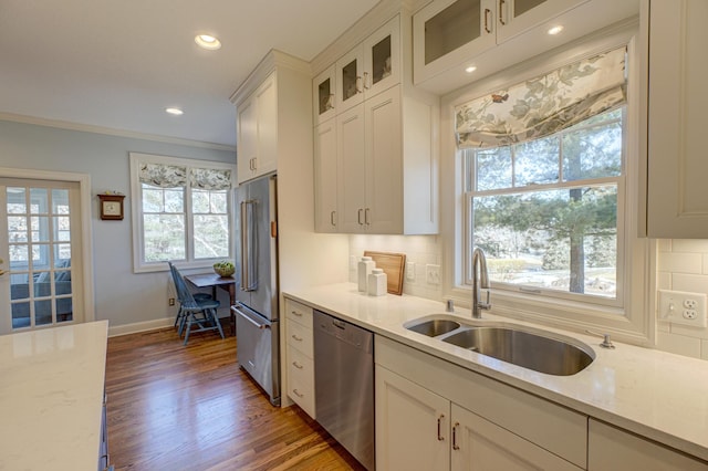 kitchen with tasteful backsplash, wood finished floors, white cabinets, stainless steel appliances, and a sink