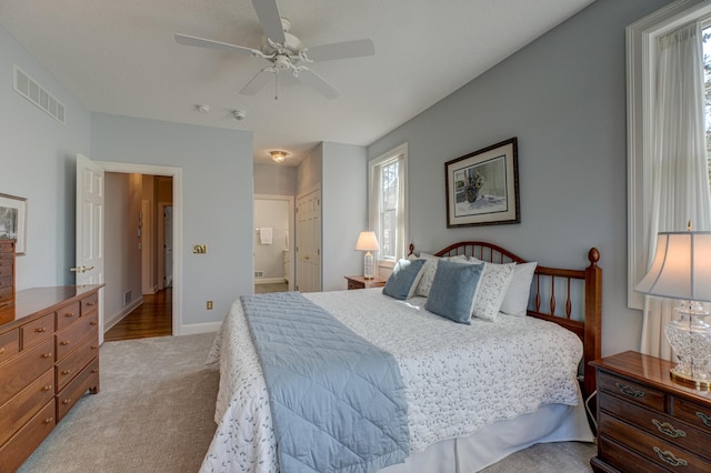 bedroom with light carpet, visible vents, multiple windows, and ensuite bathroom