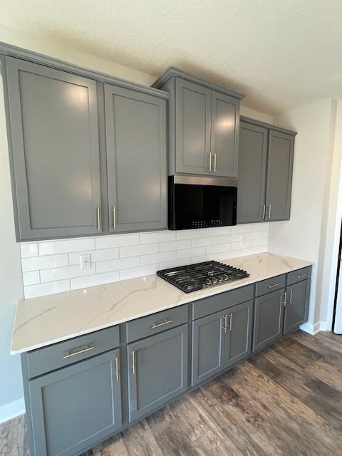 kitchen featuring dark hardwood / wood-style floors, gray cabinets, tasteful backsplash, light stone counters, and gas cooktop