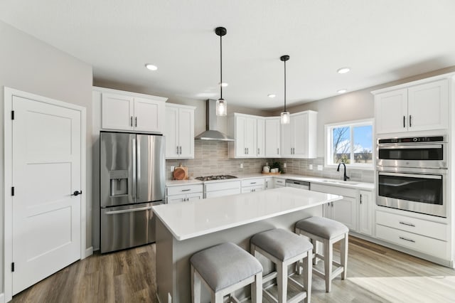 kitchen featuring white cabinetry, a center island, wall chimney exhaust hood, stainless steel appliances, and sink