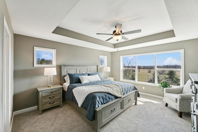 bedroom featuring light carpet, a textured ceiling, a raised ceiling, and ceiling fan