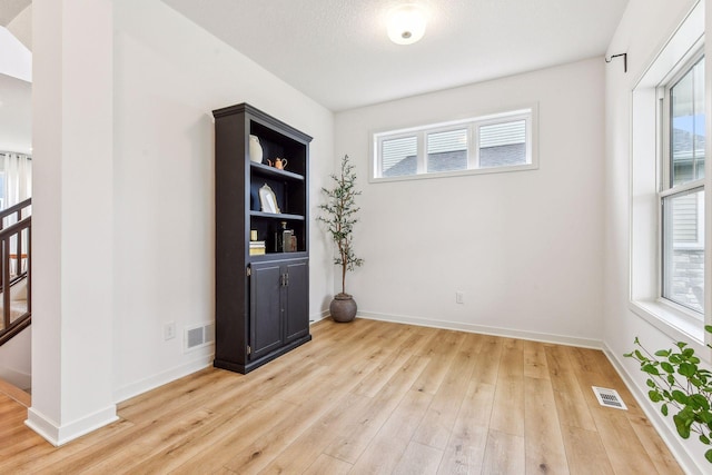 spare room featuring light wood-style flooring, stairway, visible vents, and baseboards