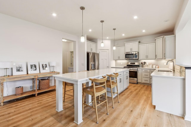 kitchen with stainless steel appliances, light countertops, decorative backsplash, light wood-style floors, and a sink