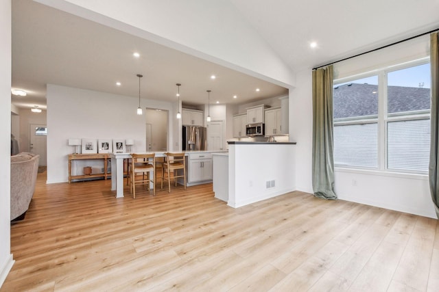 kitchen with lofted ceiling, light wood-style floors, appliances with stainless steel finishes, and open floor plan