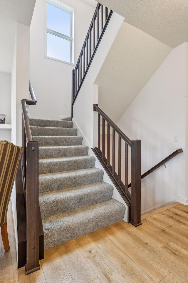 staircase featuring lofted ceiling, baseboards, and hardwood / wood-style floors