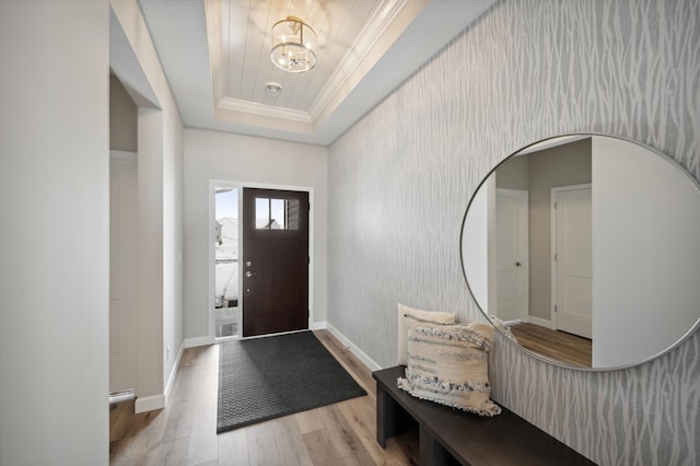 entrance foyer with a tray ceiling, ornamental molding, and light wood-type flooring