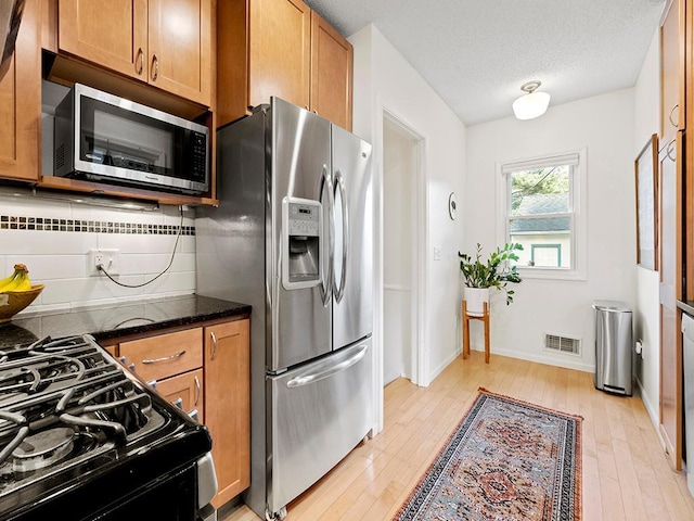 kitchen featuring tasteful backsplash, dark stone countertops, light hardwood / wood-style floors, a textured ceiling, and appliances with stainless steel finishes