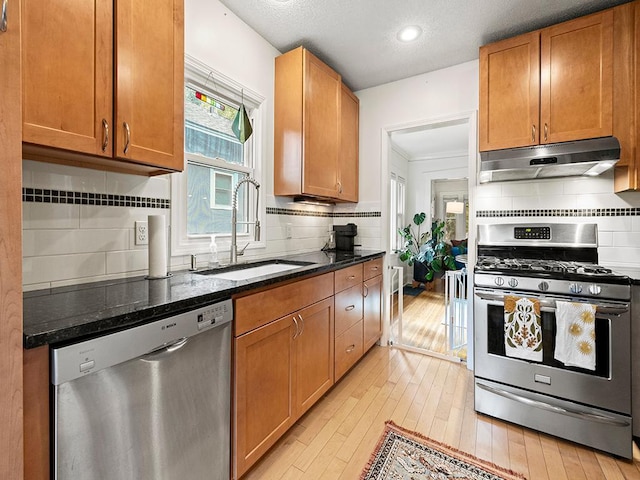 kitchen featuring sink, stainless steel appliances, light hardwood / wood-style flooring, backsplash, and dark stone counters