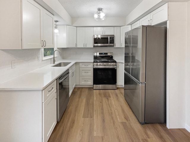 kitchen with white cabinetry, sink, a textured ceiling, appliances with stainless steel finishes, and light wood-type flooring