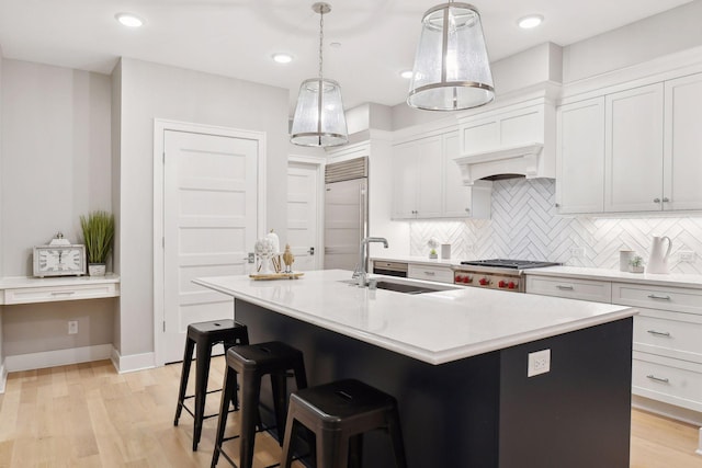 kitchen with sink, stainless steel appliances, decorative light fixtures, a center island with sink, and light wood-type flooring