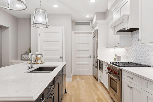 kitchen featuring white cabinetry, sink, premium appliances, light hardwood / wood-style floors, and pendant lighting