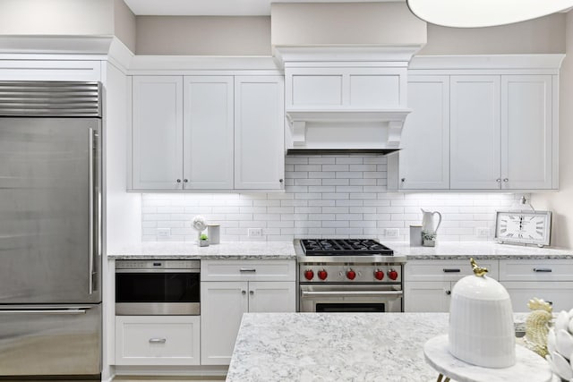 kitchen with decorative backsplash, high end appliances, and white cabinets