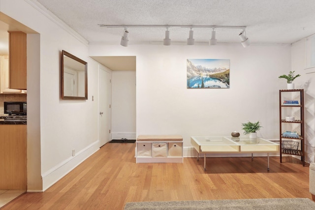 interior space with rail lighting, ornamental molding, a textured ceiling, and light wood-type flooring