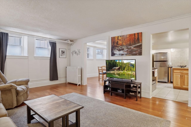 living room with a healthy amount of sunlight, light wood-type flooring, radiator heating unit, and a textured ceiling