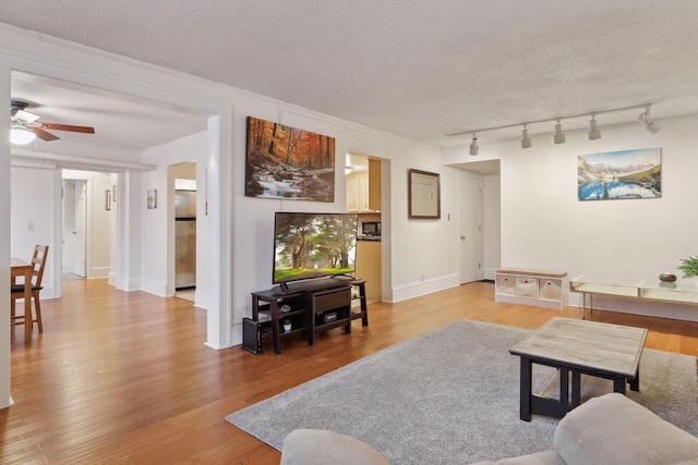 living room with ceiling fan, rail lighting, a textured ceiling, and hardwood / wood-style flooring