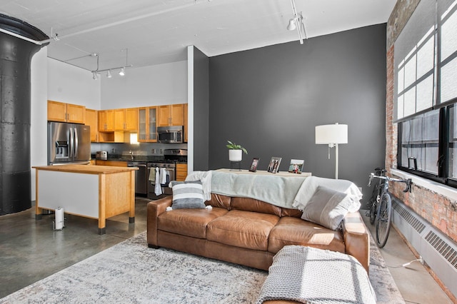 living room featuring radiator heating unit, a towering ceiling, concrete floors, and track lighting