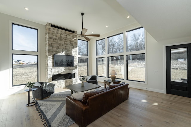 living room featuring a stone fireplace, light hardwood / wood-style floors, ceiling fan, and a high ceiling