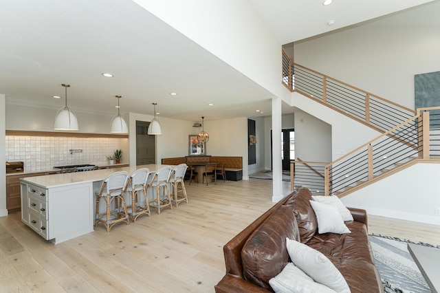 kitchen with a kitchen bar, tasteful backsplash, light stone counters, decorative light fixtures, and light wood-type flooring