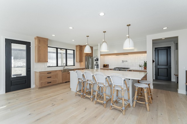 kitchen with a spacious island, sink, decorative light fixtures, light hardwood / wood-style flooring, and stainless steel appliances