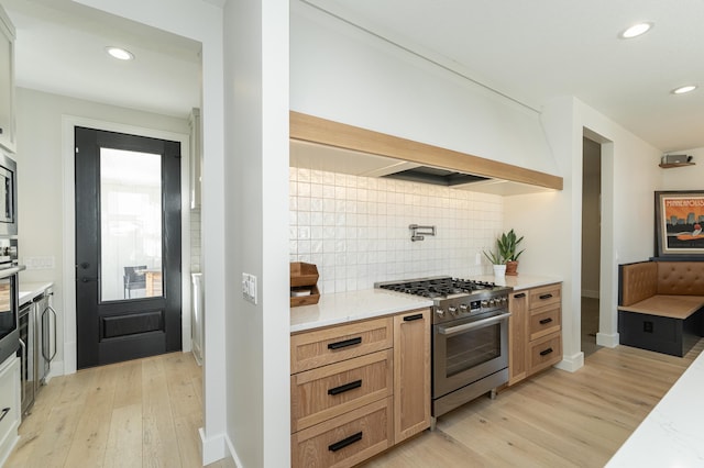 kitchen featuring premium range hood, appliances with stainless steel finishes, light hardwood / wood-style flooring, and decorative backsplash