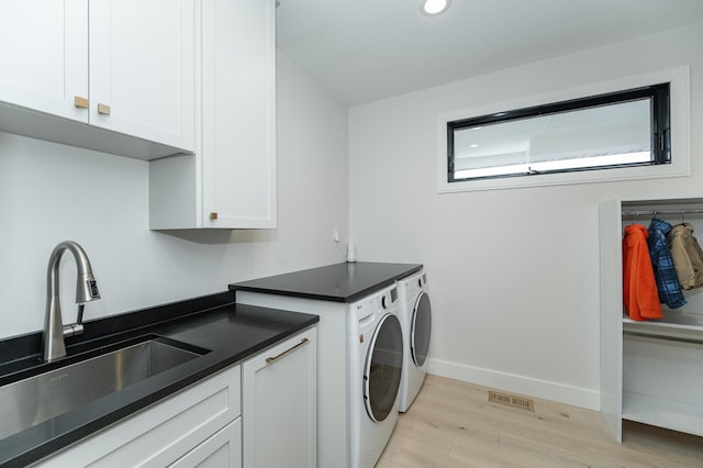 laundry area with cabinets, washing machine and clothes dryer, sink, and light hardwood / wood-style flooring