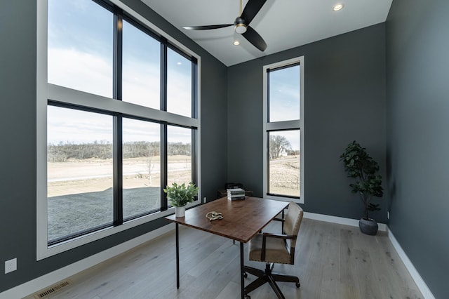 office area with a towering ceiling, light hardwood / wood-style flooring, and ceiling fan