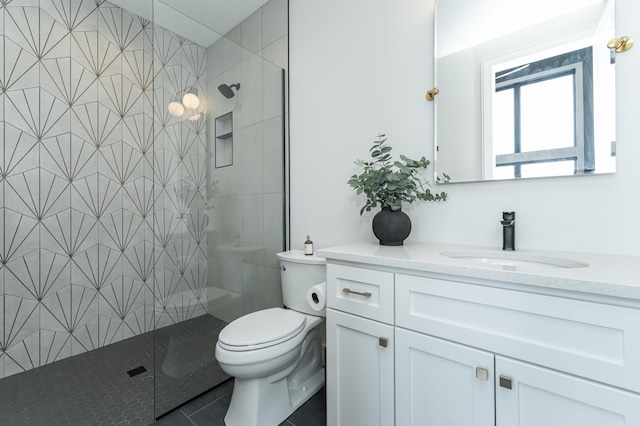 bathroom with tile patterned flooring, vanity, a tile shower, and toilet