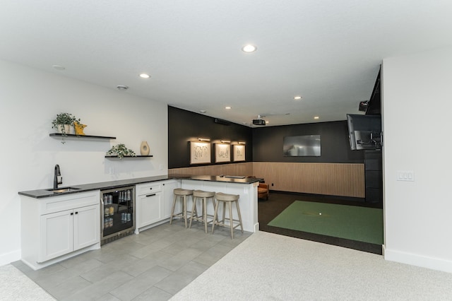 kitchen featuring wine cooler, sink, white cabinetry, a kitchen breakfast bar, and kitchen peninsula