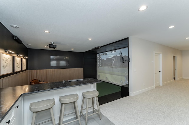 interior space with white cabinetry, a kitchen bar, light carpet, and a textured ceiling