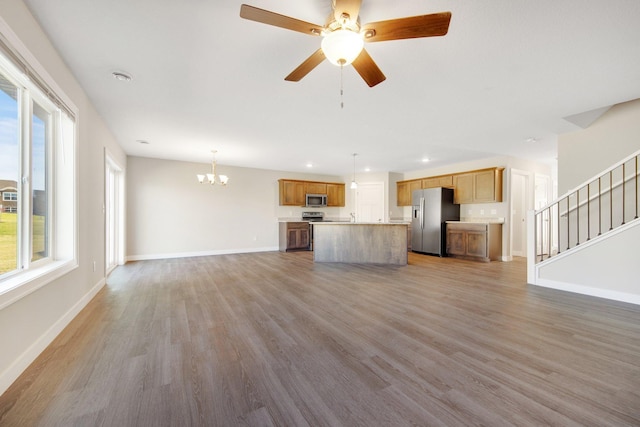 unfurnished living room featuring a healthy amount of sunlight, ceiling fan with notable chandelier, and hardwood / wood-style flooring