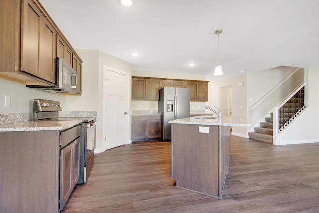 kitchen featuring dark hardwood / wood-style flooring, an island with sink, pendant lighting, and appliances with stainless steel finishes