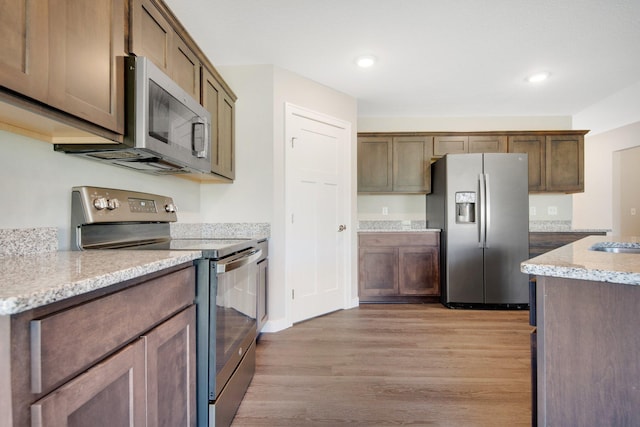 kitchen featuring light stone countertops, light wood-type flooring, stainless steel appliances, and sink